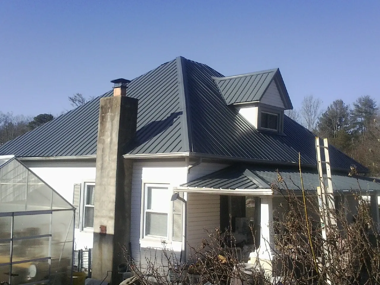 Dark blue standing seam metal roof on a white farmhouse with dormer — Slate & Tile Roof Repair by Roofing Brothers in Westlake