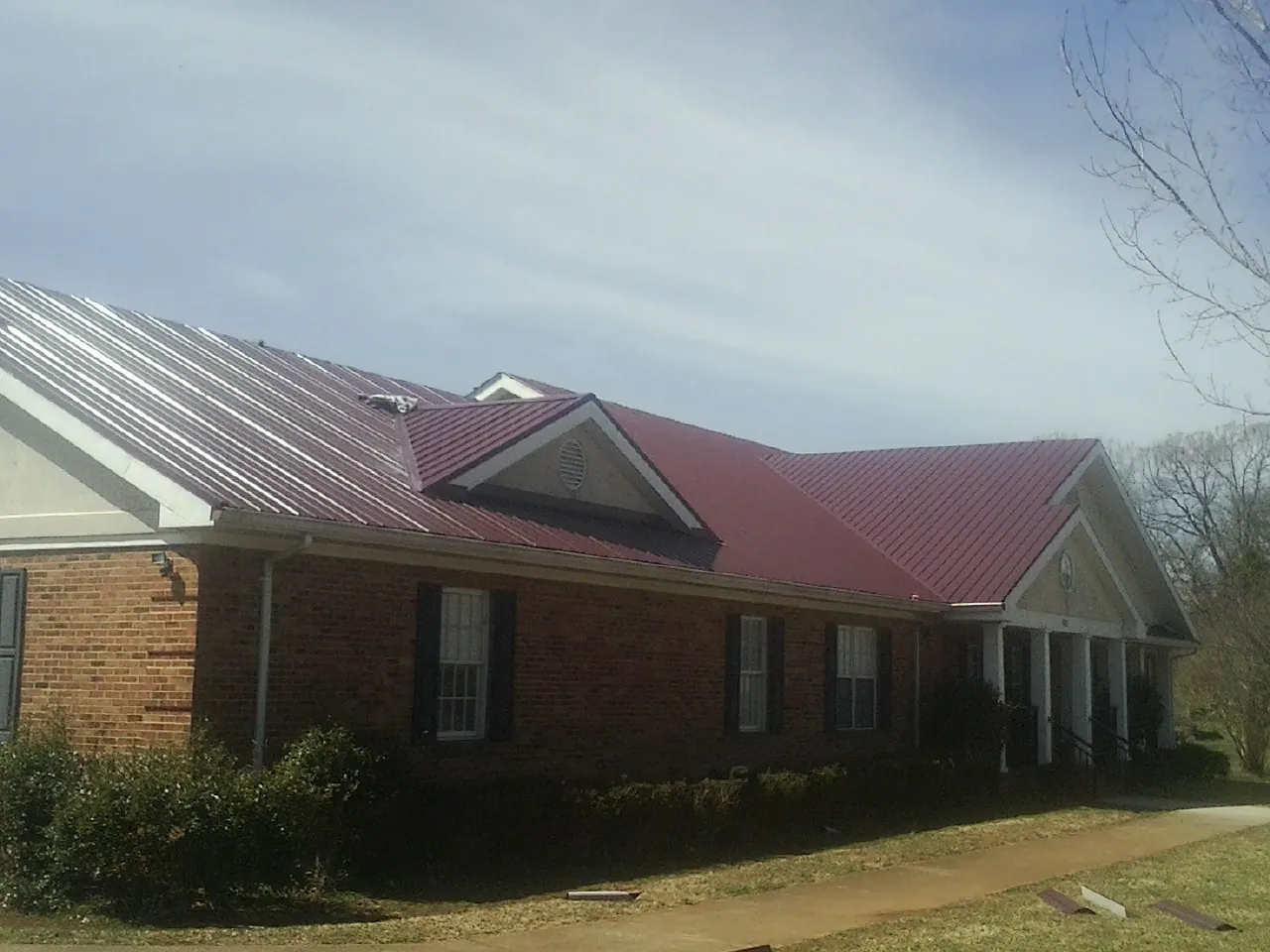 Red metal roof with gabled entries on a long brick building, from a Hail Damage Roof Repair job in Westlake