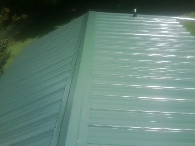 New green metal panels meeting at the ridge of a roof — Flat Roof Repair work by our crew in Westlake