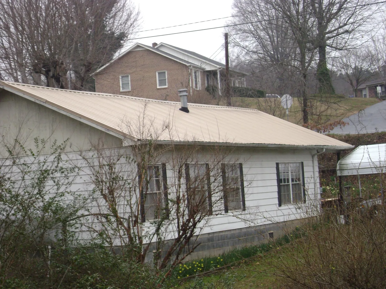 Tan metal roof on a white sided house set into a hillside — Commercial Roofing by Roofing Brothers in Westlake
